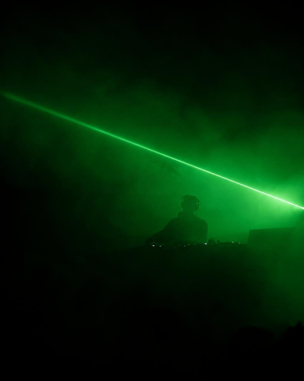 DJ ante su mesa de mezclas bajo un haz de luz verde